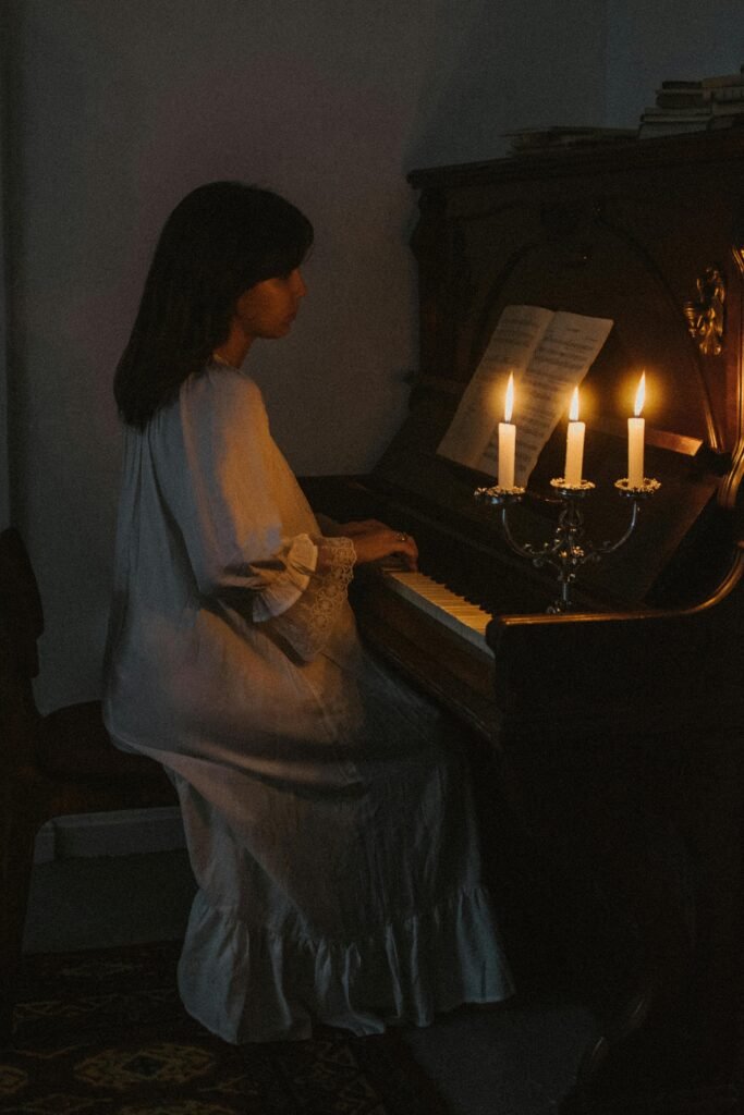 A woman elegantly plays the piano in a dimly lit room with candlelight ambiance.