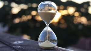 An hourglass with sand on a ledge set against a sunset background, symbolizing time passage.
